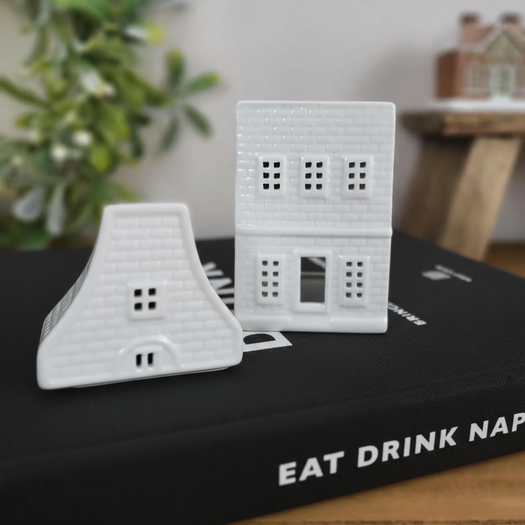 Two white 3D-printed house models on a book with a blurred indoor background.